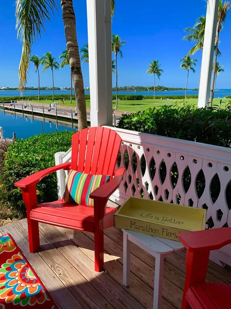 Red Adirondack chair on the deck beside a Life is Better on Marathon, Florida sign, overlooking the water.