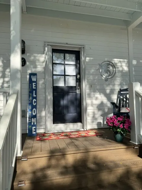 Navy front door with a Welcome, Living on Island Time sign, a marlin wall sculpture, and potted flowers on the porch.