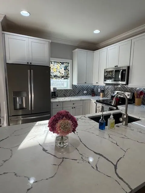 Bright white kitchen with quartz counters, stainless appliances, and a herringbone tile backsplash.